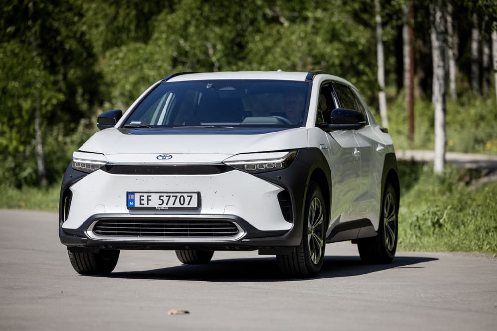 Hvit  og svart Toyota BZ4X foran grønne trær